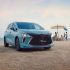 A light blue MPV is parked on a sandy beach, with the sea and a family enjoying the shore in the background, highlighting its stylish design and family-friendly appeal.