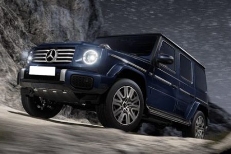 The Mercedes-Benz G-Class SUV, in a deep blue finish, navigates rocky terrain under a starry night sky, showcasing its iconic off-road capability, bold design, and luxury engineering.