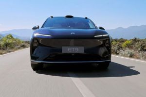 Dark NIO ET9 electric car: front view, driving on road with mountain/vegetation backdrop under blue sky.