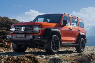 An orange off - road SUV parked on a rocky mountain terrain under a blue sky with white clouds.