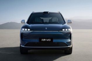 The AITO M9 SUV, in a sleek blue finish, stands on an open plain with mountains in the background, showcasing its modern design and advanced autonomous driving sensor array.