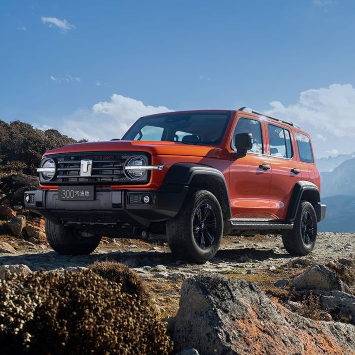 An orange off - road SUV parked on a rocky mountain terrain under a blue sky with white clouds.
