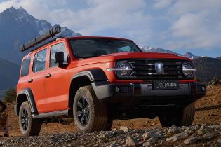 A red off - road SUV parked on a rocky mountain terrain with snow - capped mountains in the background.