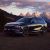 A dark - colored Xpeng G9 SUV parked with a stunning mountain range and a colorful sunset sky in the background.