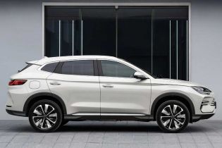A white SUV with a sleek side profile, featuring stylish alloy wheels and a streamlined body, parked in front of a modern building with large glass windows.