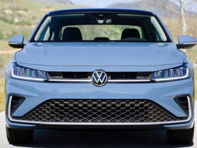 Front view of light blue Volkswagen car: iconic VW logo, sleek LED headlights, grille, on road with green hills.