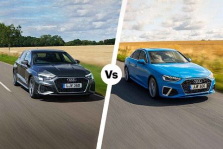 Two Audi sedans (black vs bright blue) on a rural road: side-by-side "vs" comparison. Both modern, sleek models (likely A3/A4 variants) driving through countryside with fields/trees in background. License plates: LJV 360 (black), JJF 500 (blue).