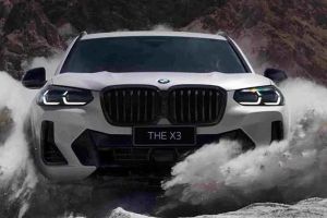 Front view of a white BMW X3 ("THE X3" badge) driving through splashing water in a rugged, mountainous area, highlighting its off-road capability and bold design.