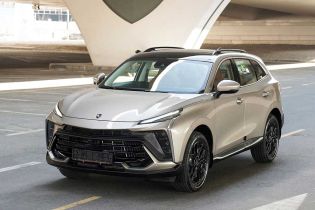 A silver SUV with a black roof, featuring a bold grille and sleek design, parked on a paved area under a modern architectural structure, highlighting its stylish and dynamic appearance.