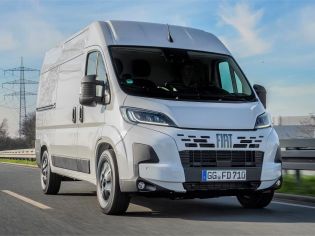 A white Fiat Ducato driving on a road under a blue sky.