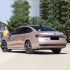 Rear side view of a pink Volkswagen Passat sedan parked on a road, with trees and a building in the background.