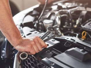 Mechanic's hand using a wrench to work on a car engine, performing maintenance, repair, or diagnostic service in an auto shop.