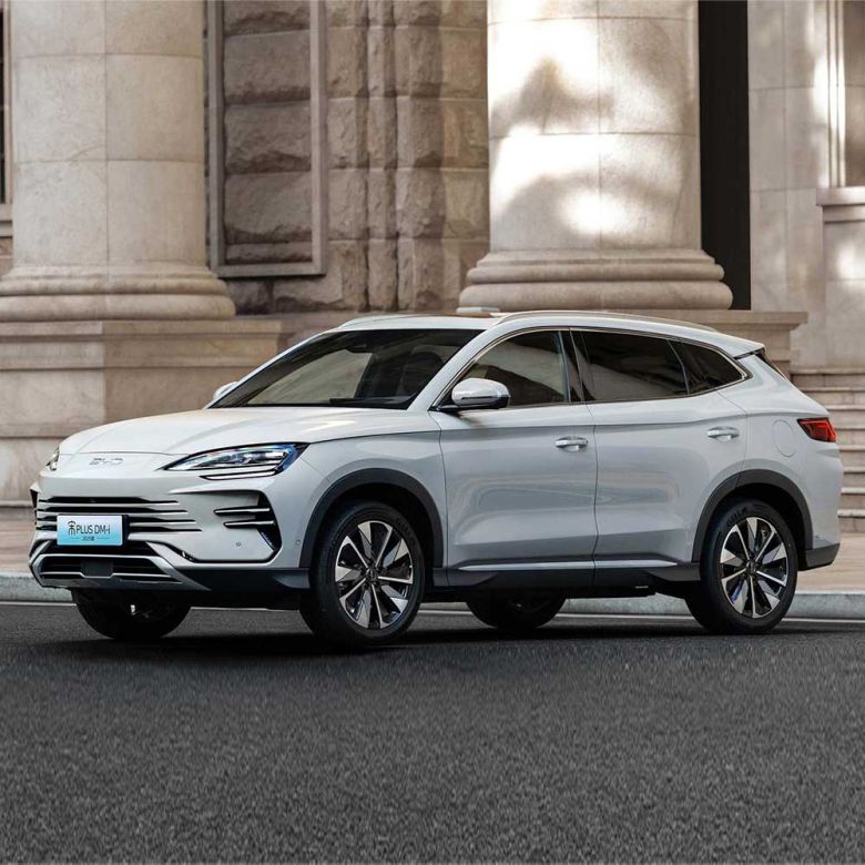 Side view of BYD Song Plus DM-i 2025 model, a light gray SUV with sleek design, parked on a road in front of a grand stone building, showcasing its elegant exterior.