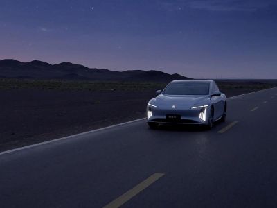A light blue electric sedan with a sleek, modern design, featuring a black roof, distinctive headlights, and black alloy wheels, presented against a plain white background.