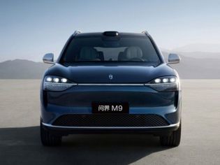 The AITO M9 SUV, in a sleek blue finish, stands on an open plain with mountains in the background, showcasing its modern design and advanced autonomous driving sensor array.
