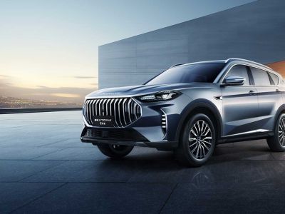 A silver Jetour X70 PLUS SUV parked on a modern, sleek pavement with a minimalist architectural background and a scenic sunset view.