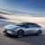 A silver Xpeng P7+ electric car parked on a paved area with a clear blue sky and distant mountains in the background.