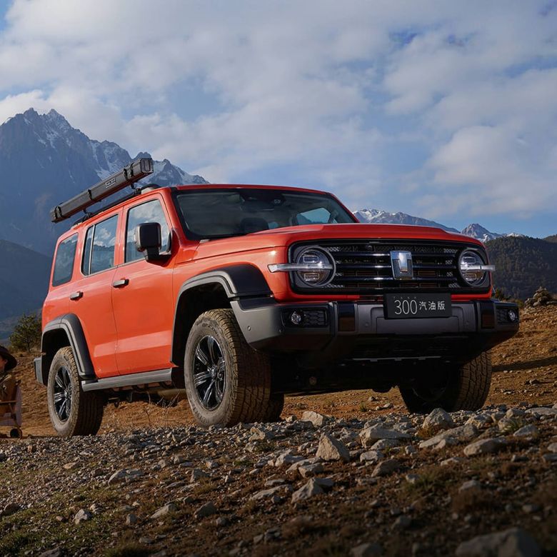 A red off - road SUV parked on a rocky mountain terrain with snow - capped mountains in the background.