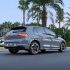 Rear side view of a gray Volkswagen Golf driving on a road, with palm trees and greenery in the background.