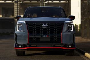Front view of a bold Nissan pickup truck, featuring a large black V-motion grille, angular LED headlights, and striking red accent trim.