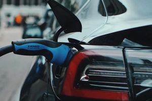 Close - up of an electric car being charged with a blue charging plug.