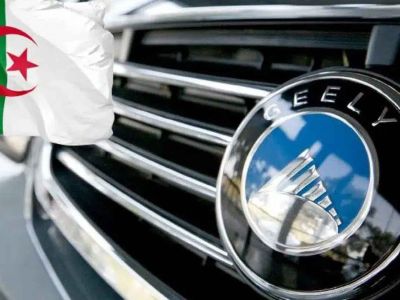 Close-up of a Geely car emblem on a grille, paired with the Algerian flag in the background, linking the automaker to Algeria.