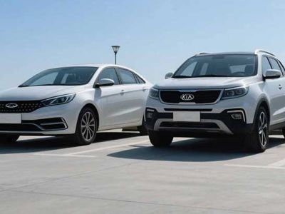 Two white cars, a sedan and an SUV, parked in an open area under a clear blue sky.
