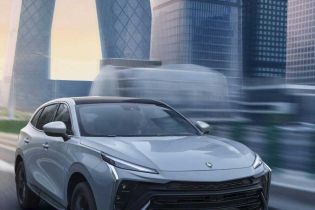 A silver T5 HEV SUV driving on a city road, with modern skyscrapers (including the iconic CCTV building) in the background, showcasing its dynamic design and urban appeal.