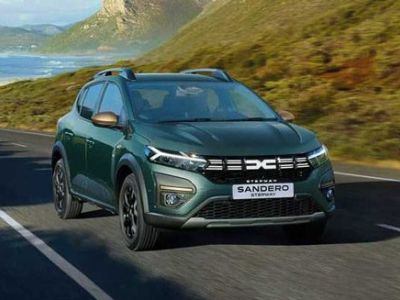 A green Dacia Sandero Stepway driving on a road by the seaside with a scenic background.