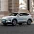 Side view of BYD Song Plus DM-i 2025 model, a light gray SUV with sleek design, parked on a road in front of a grand stone building, showcasing its elegant exterior.