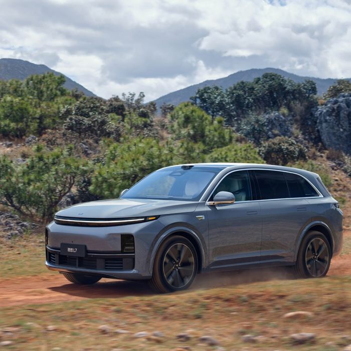 A gray Li Auto L7 driving on a dirt road with mountains and trees in the background.