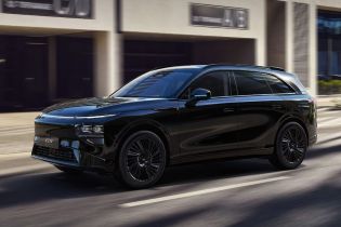 A black Xpeng G9 SUV driving on a city street with modern buildings in the background.