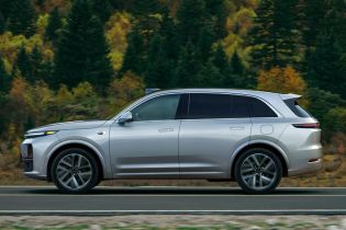 A silver SUV driving on a road with a forest in the background.