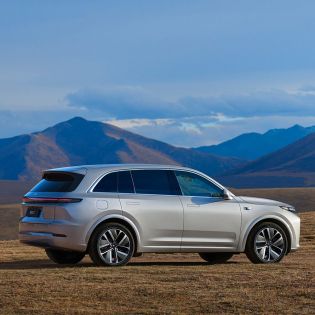 A silver SUV parked on a grassland with mountains in the background.