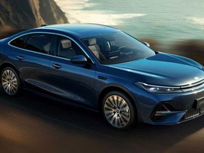 A blue Geely Galaxy A7 sedan driving on a coastal road, with the ocean and cliffs in the background, showcasing its sleek design and dynamic performance.