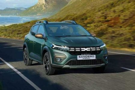 A green Dacia Sandero Stepway driving on a road by the seaside with a scenic background.