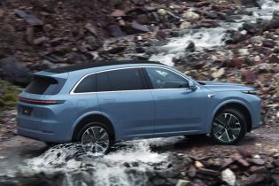 A light blue SUV driving through a stream with rocky terrain in the background.