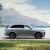 A silver SUV parked by a lake with mountains in the background.