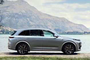 A silver SUV parked by a lake with mountains in the background.