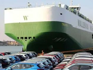 A large green and white Wallenius Wilhelmsen ship docked at a port with many cars parked nearby.
