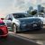 Toyota Corolla 2024 (including a gray Corolla Intelligent Electric Hybrid) driving on the road with a cityscape in the background.