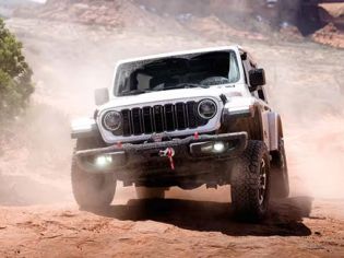Front view of a white 2026 Jeep Wrangler driving in the sand