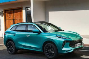 A turquoise Fengxing T5 EVO SUV parked on a crosswalk, with a modern building featuring a blue roof and wooden door in the background, highlighting its sleek side design.