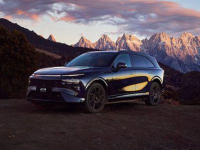 A dark blue SUV parked on a rocky terrain, with majestic mountains and a colorful sunset sky in the background, highlighting its sleek design and scenic surroundings.