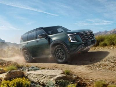 2026 Nissan Armada NISMO driving on a dirt road near some rocks and wildflowers
