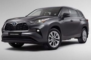 Gray Toyota Highlander SUV (side-front view), illuminated headlights, "HIGHLANDER" badge, plain light backdrop.
