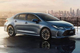 A blue Toyota Corolla car parked on a wet surface with a city skyline in the background.