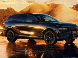 Xpeng G9 parked on reflective wet ground, set against a glowing golden desert landscape at sunset.