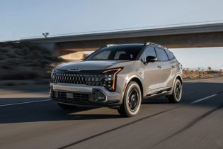 Silver Kia SUV driving on a desert highway, showcasing its bold front grille and modern design against an overpass backdrop.