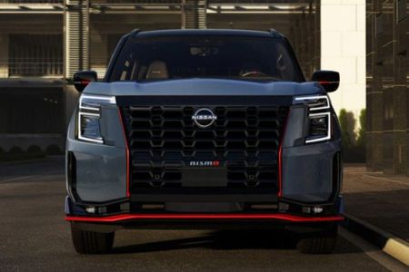 Front view of a bold Nissan pickup truck, featuring a large black V-motion grille, angular LED headlights, and striking red accent trim.